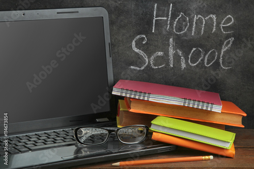 open the laptop near the books and glasses on a brown wooden table  on blackboard background with inscription 