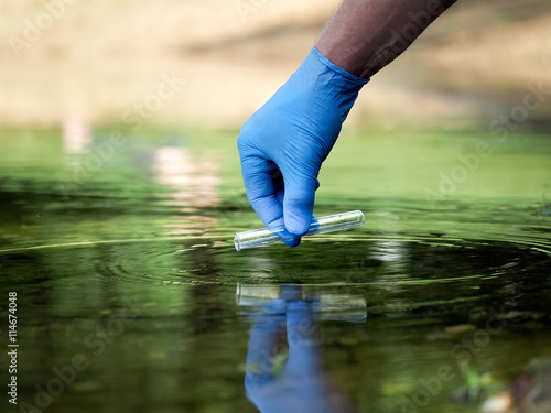 Water sample. Hand in glove collects water in a test tube. Concept - water purity analysis, environment, ecology. Water testing for infections, permission to swim 