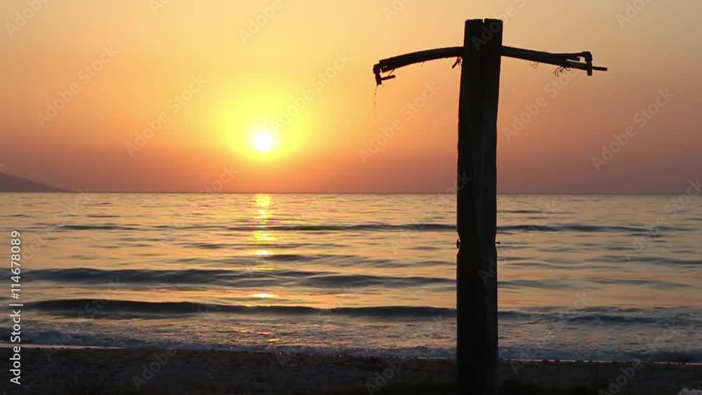 A shower dripping on the beach in silhouette at sunset, rolling waves in slow motion A shower dripping on the beach in silhouette at sunset, rolling waves in slow motion
