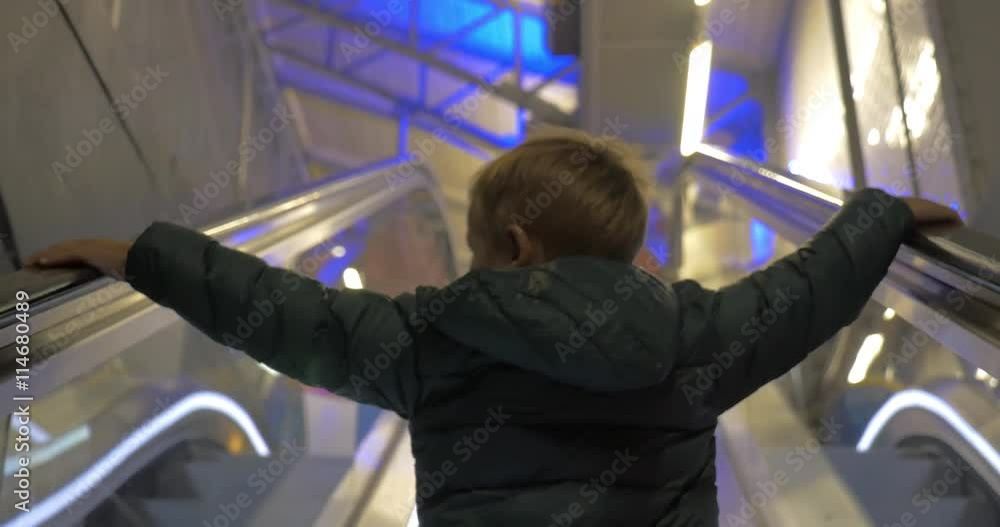 Back view of a little boy riding up on trade centre escalator with hands on rails Back view of a little boy riding up on trade centre escalator with hands on rails