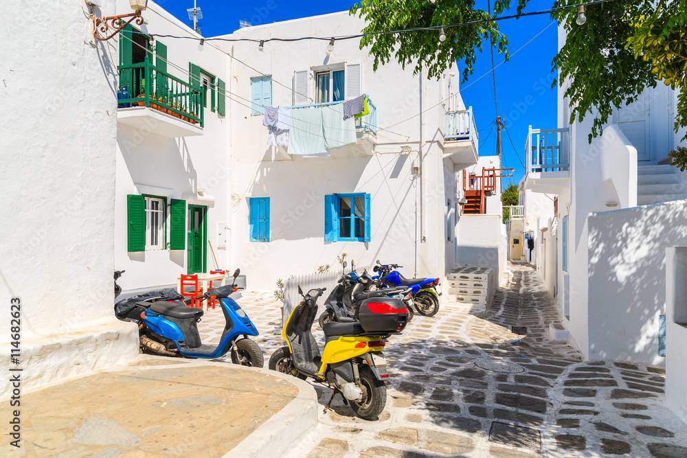 Obraz premium MYKONOS TOWN, GREECE - MAY 16, 2016: Colorful scooters parked on street in Mykonos town on island of Mykonos, Cyclades, Greece