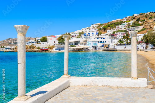 Fototapeta Naklejka Na Ścianę i Meble -  Greek columns on coastal promenade and view of beach in Mykonos town, Cyclades islands, Greece