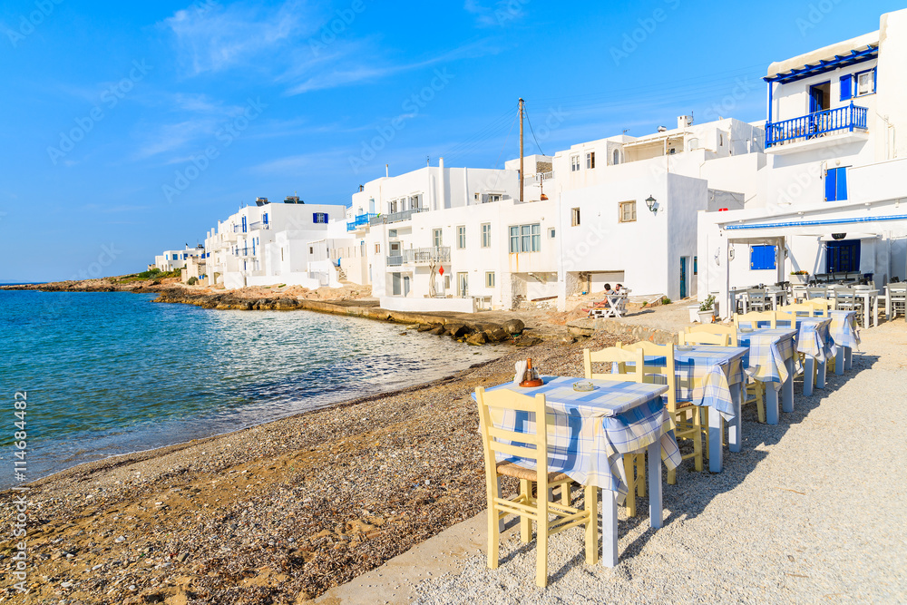 Tables of typical taverna on beach in Naoussa port with traditional white Greek architecture, Paros island, Cyclades, Greece