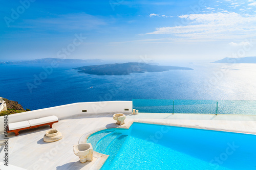 OIA VILLAGE, SANTORINI ISLAND - MAY 24, 2016: A view of caldera and luxury hotel swimming pool in foreground, typical white architecture of Imerovigli village on Santorini island, Greece.