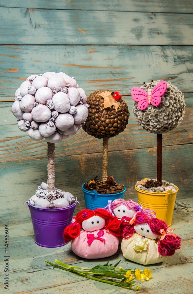Decorative topiary handmade trees, handmade dolls and flowers on table on bright wooden background