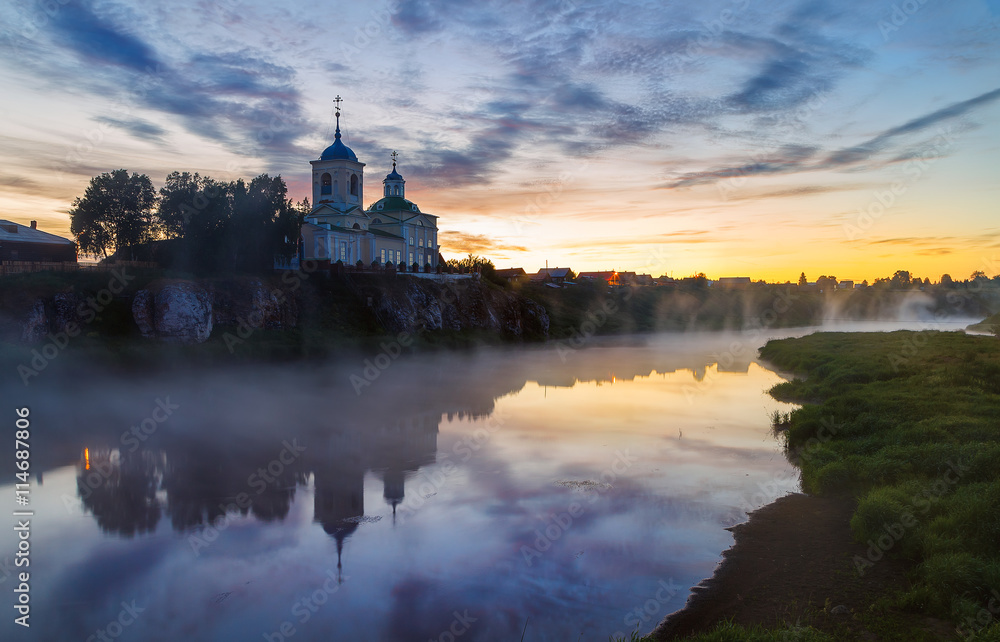 Church on a rock above the river on a background of a beautiful summer sunrise and fog. Ural village Sloboda