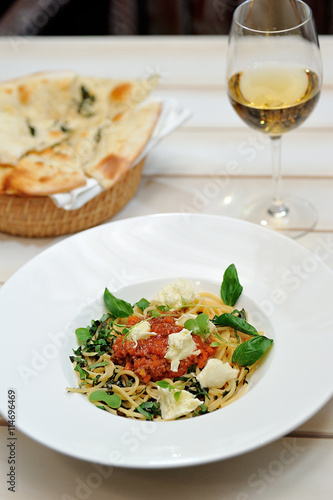 The image is very tasty spaghetti bolognese with cheese and basil on a white table.
