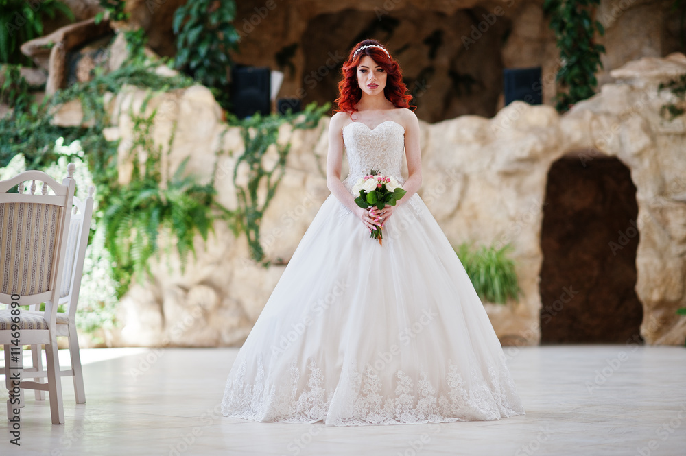 Charming red-haired bride with wedding bouquet at hand posed at