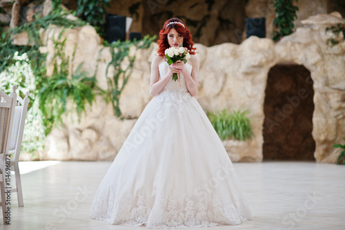 Charming red-haired bride with wedding bouquet at hand posed at