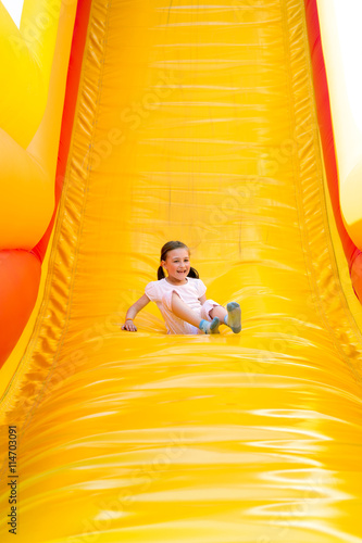 Foto Happy little girl having lots of fun on a jumping castle while sliding