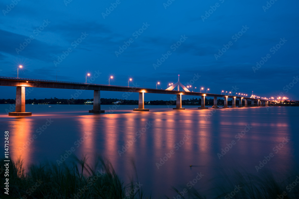 View of the concrete bridge with golden light reflection on water surface at night time