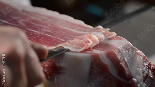 Butcher cuts a slice of Parma ham with a knife, close up on the slice and knife