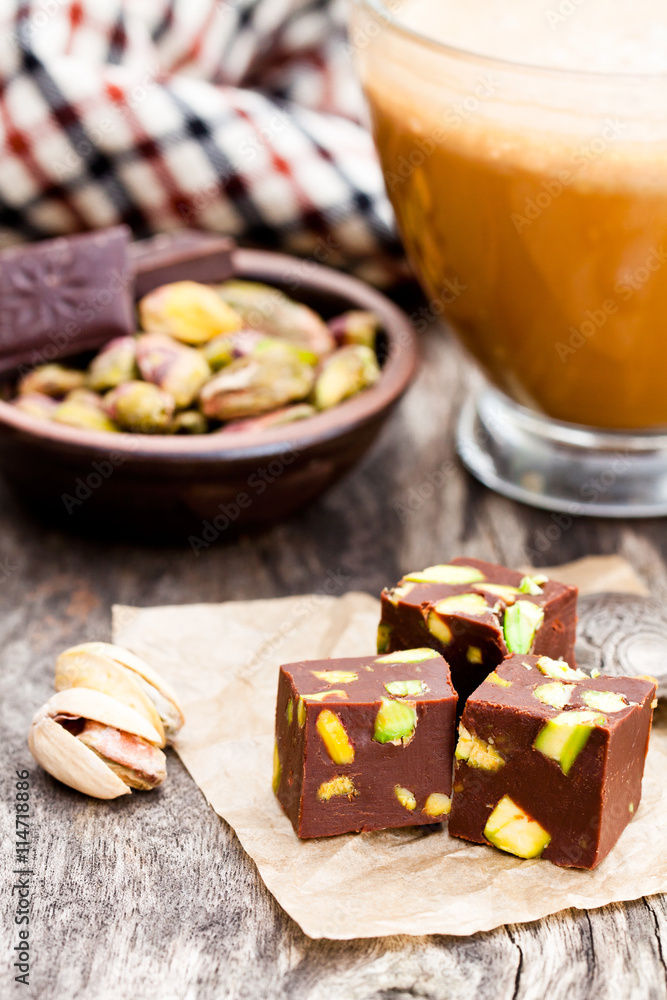 Fototapeta premium Dark chocolate cubes with pistachios and cup of coffee on woode