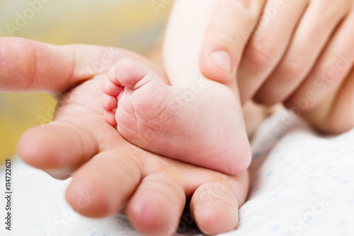 Father holds in his hands a little foot of newborn baby.