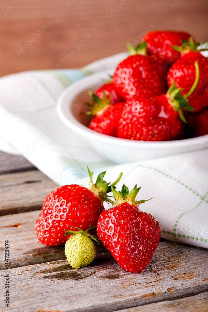 Green strawberry with red ones next to bowl Green strawberry with red ones next to bowl