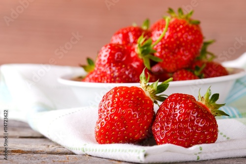 Red fresh strawberries on cloth in front of bowl
