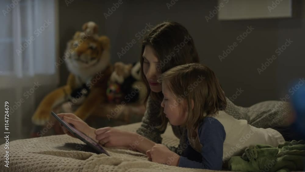 Medium panning shot of mother reading e-book to son on bed / Cedar Hills, Utah, United States Medium panning shot of mother reading e-book to son on bed / Cedar Hills, Utah, United States