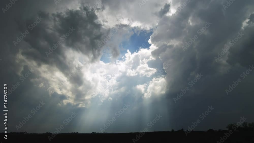 Sun rays through time-lapse white and stormy gray clouds sweep across the landscape Sun rays through time-lapse white and stormy gray clouds sweep across the landscape