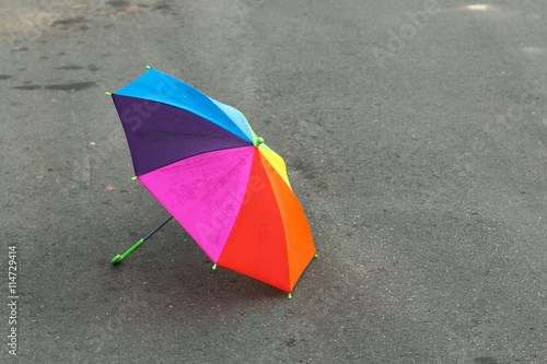 Rainbow umbrella lying on the pavement after the summer rain, forgotten by a child. Sadness and loneliness.