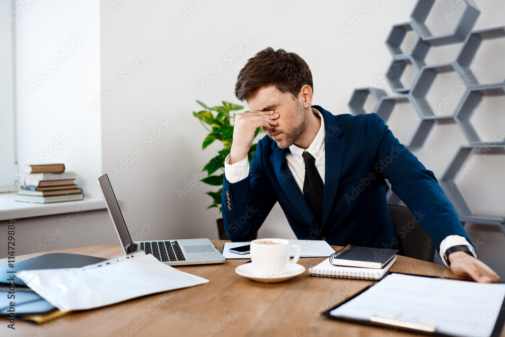 Upset young businessman sitting at workplace, office background. Upset young businessman sitting at workplace, office background.