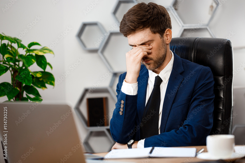 Fototapeta premium Upset young businessman sitting at workplace, office background.