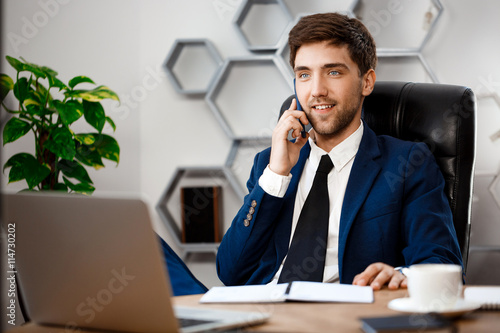 Young successful businessman speaking on phone, office background.