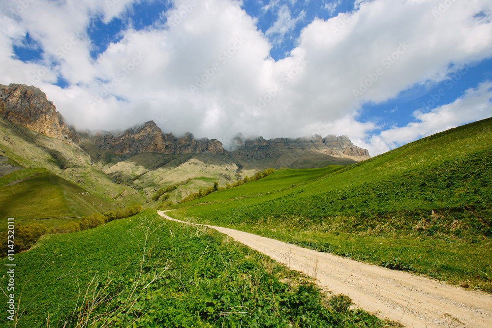 Landscape with dirt road in the mountains under a cloudy sky