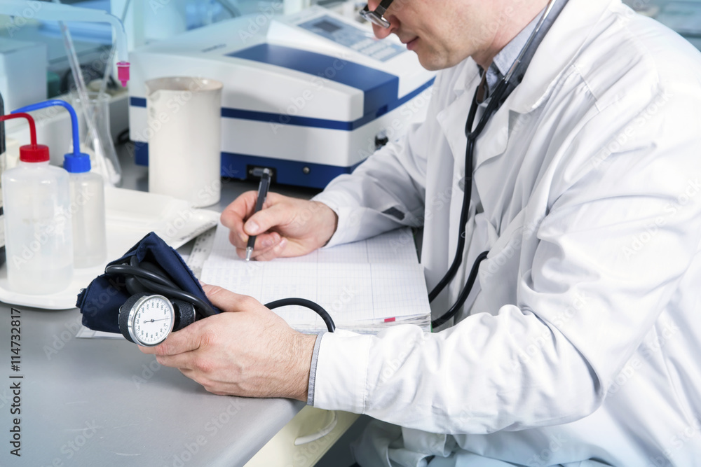 Doctor with stethoscope, glasses and robe write on table in laboratory Doctor with stethoscope, glasses and robe write on table in laboratory