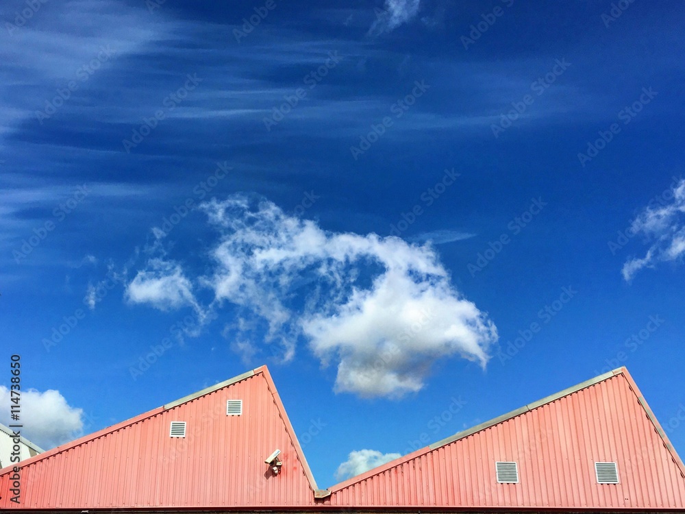 Red industrial building in triangle shape with blu sky and white clouds