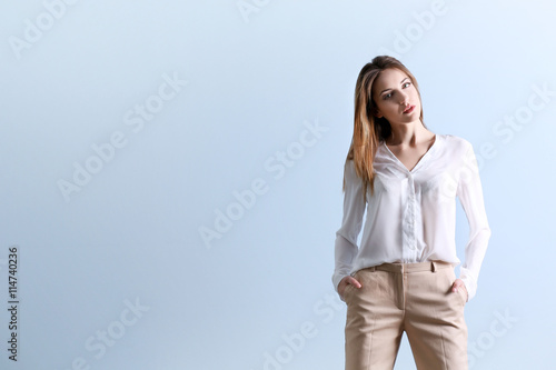 Beautiful young woman in a white shirt and beige pants on blue wall background © Africa Studio