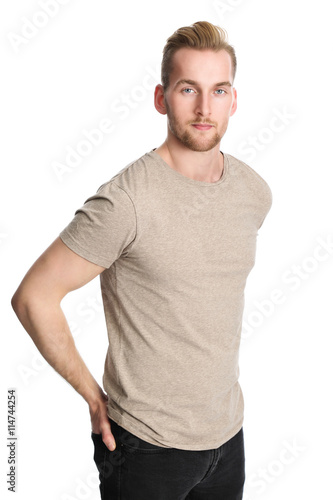 One man standing wearing a beige tshirt, standing in front of a white background looking at camera.