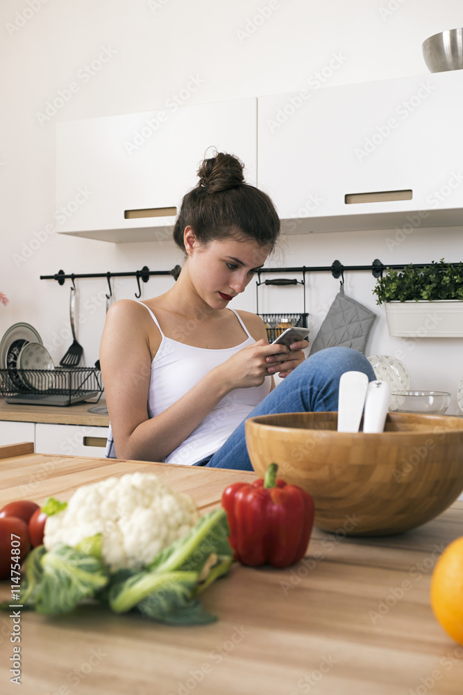 Portrait of young woman using phone at table with vegetables