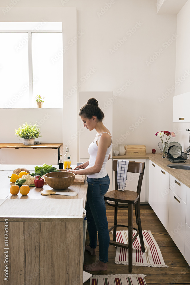 Young woman preparing salad in kitchen