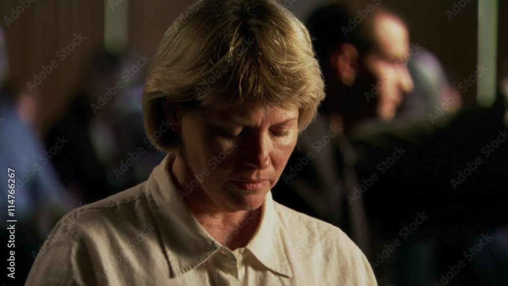 Close view of woman with head bowed in prayer, other praying people in background Close view of woman with head bowed in prayer, other praying people in background