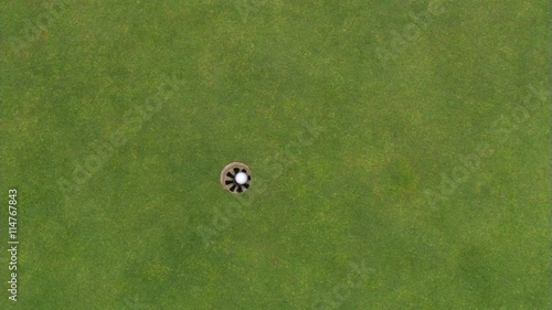 Overhead shot of hole on green and golf ball going in