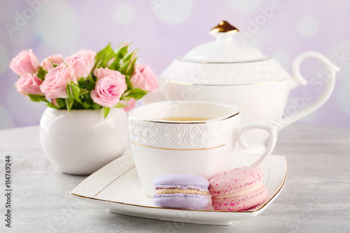 Cup of tea with macaroons and roses on wooden table