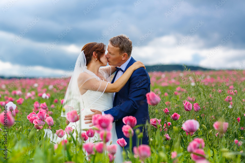 Happy wedding couple in pink poppy field Happy wedding couple in pink poppy field