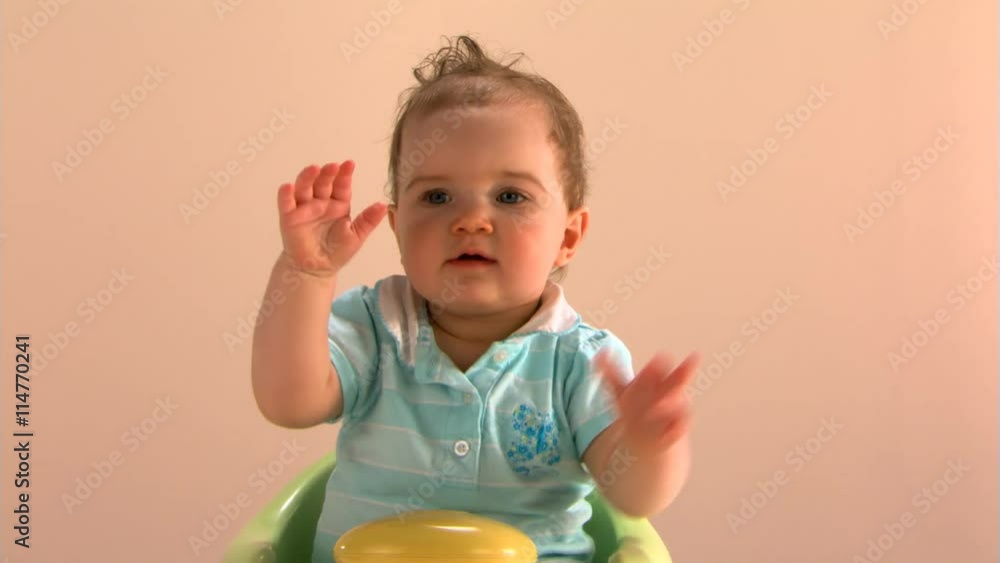 Baby girl sitting in a baby chair and waving Baby girl sitting in a baby chair and waving