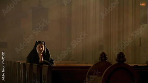 Praying nun kneeling among sun rays in empty church photo