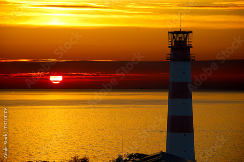 Red Lighthouse with Light Beam at Sunset.