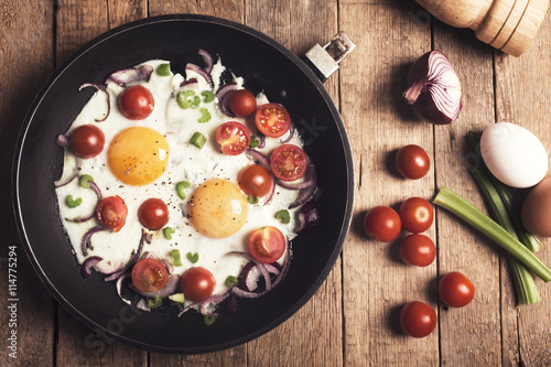 Fried eggs with vegetables on the rustic wooden table