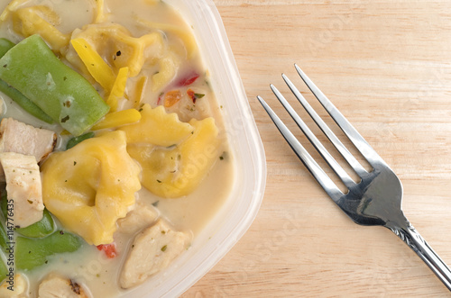 Chicken and tortellini TV dinner on a table with a fork to the side.