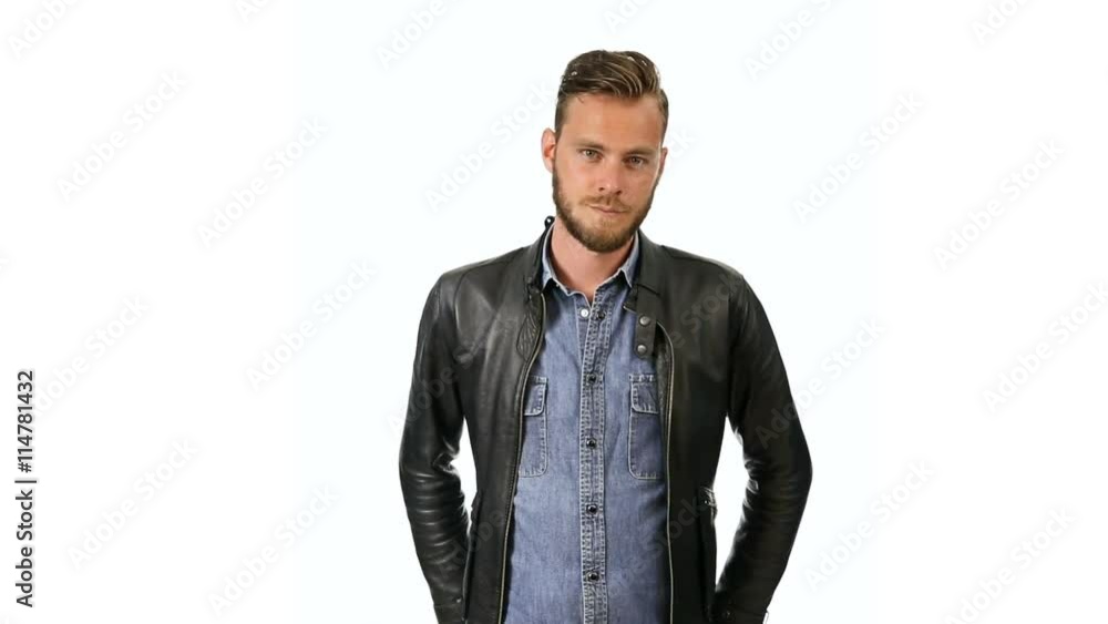 A fashionable man wearing a jeans shirt with a black leather jacket standing against a white background looking at camera. A fashionable man wearing a jeans shirt with a black leather jacket standing against a white background looking at camera.