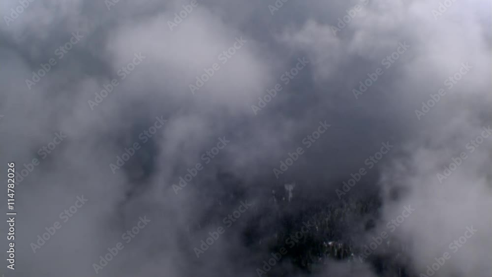 Flight through blowing vapor above forested snowy ridge into blue sky, passenger POV Flight through blowing vapor above forested snowy ridge into blue sky, passenger POV