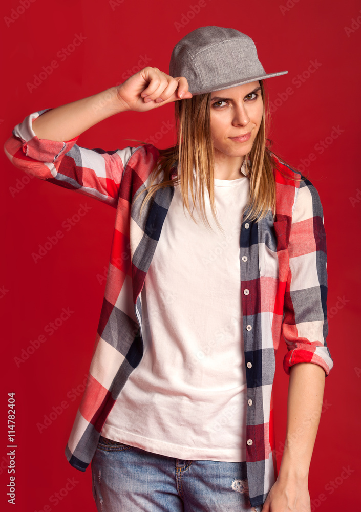 Beautiful cool hipster girl fashion posing in shirt and cap on a red background Beautiful cool hipster girl fashion posing in shirt and cap on a red background