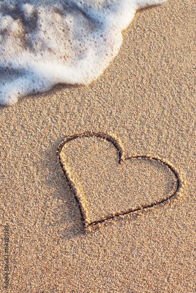 heart symbol handwritten on sandy beach with soft ocean wave