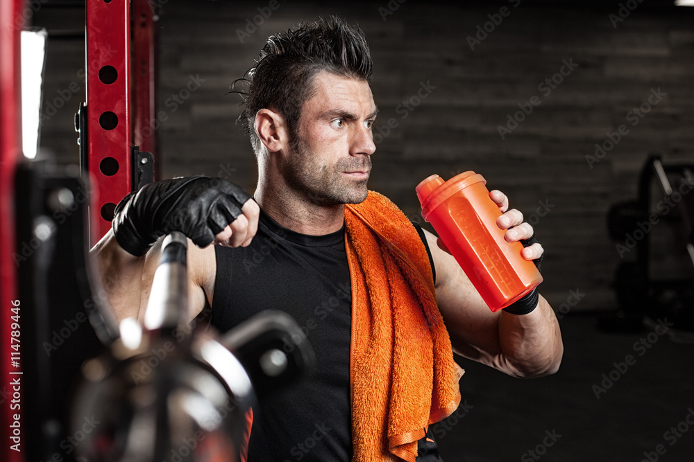 Naklejka premium Muscular bodybuilder guy doing exercises with dumbbells in gym