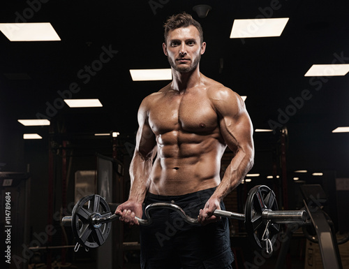 Muscular bodybuilder guy doing exercises with dumbbells in gym