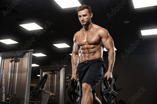 Muscular bodybuilder guy doing exercises with dumbbells in gym