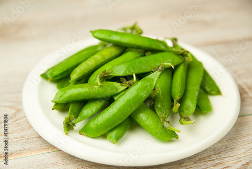 Green pea pods on the big white plate.